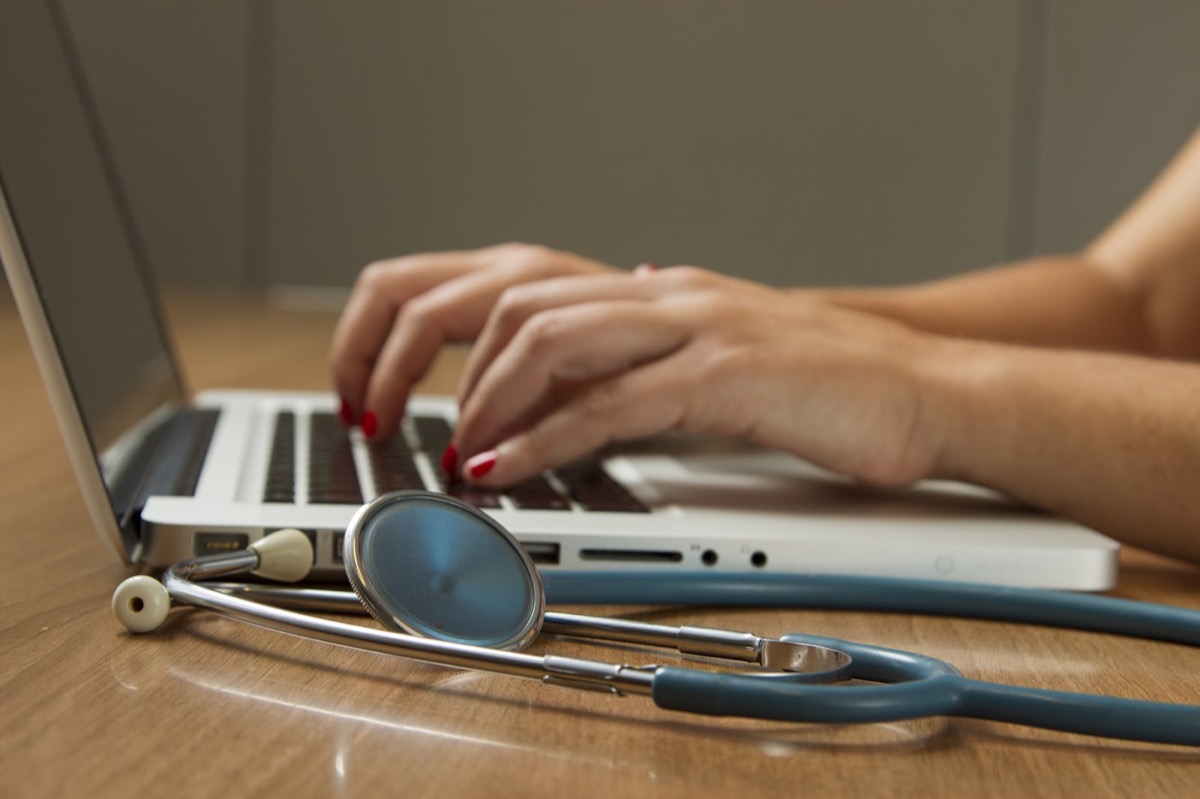 A clinician reviewing patient information on a laptop, a stethoscope on the desk beside them.